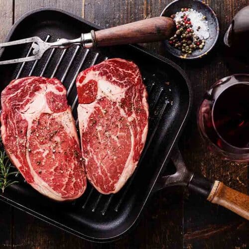 Two rib eye steaks raw on grill with seasonings