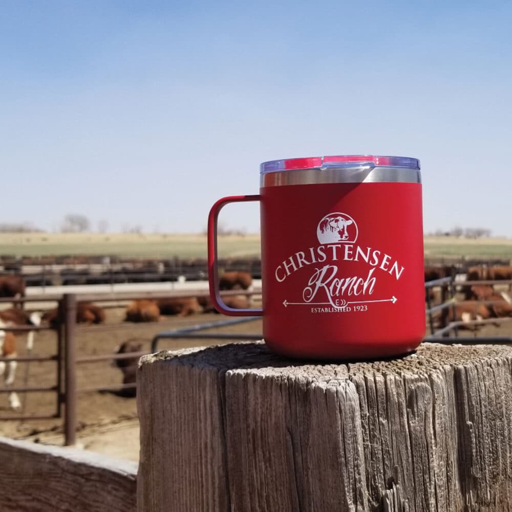 Christensen Ranch camping mug on a fence post with barn and corrals in the background