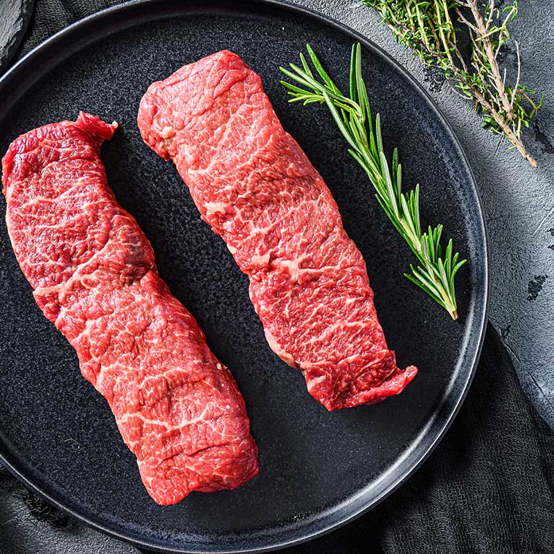 Two Denver steaks in pan with herbs
