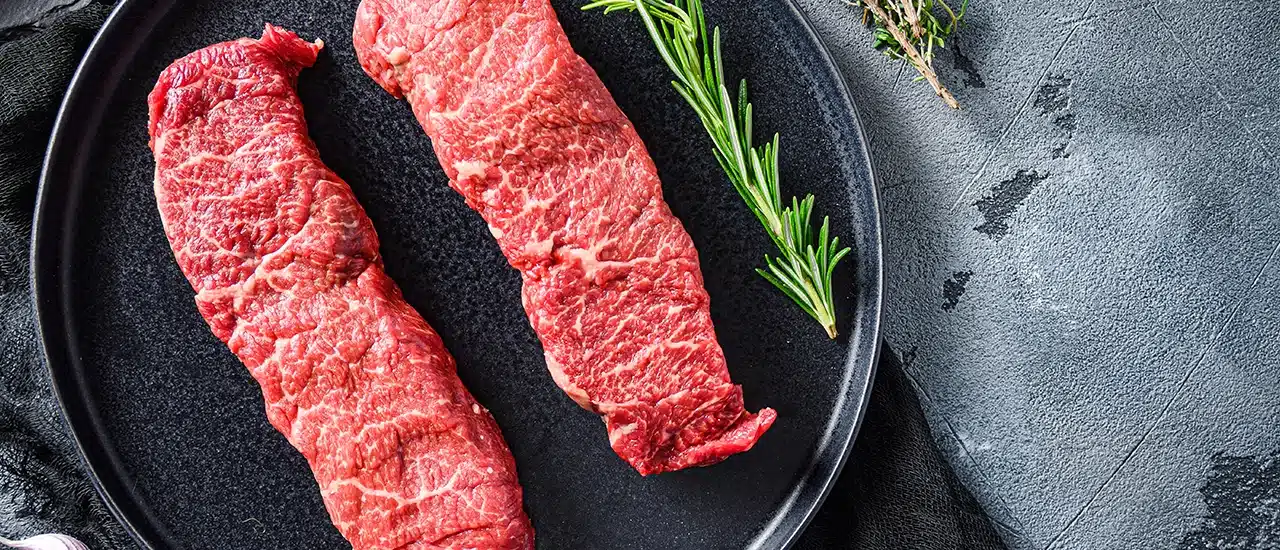 Two raw Denver steaks on metal tray with garnish