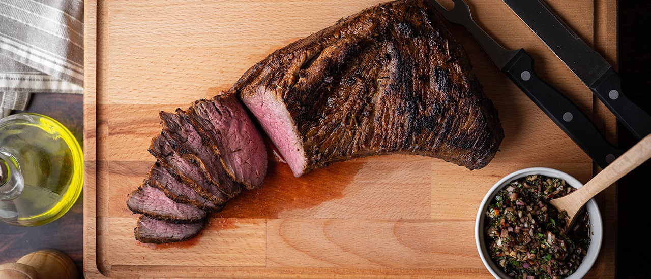 Grilled tri tip steak on wooden cutting board with olive oil and seasonings